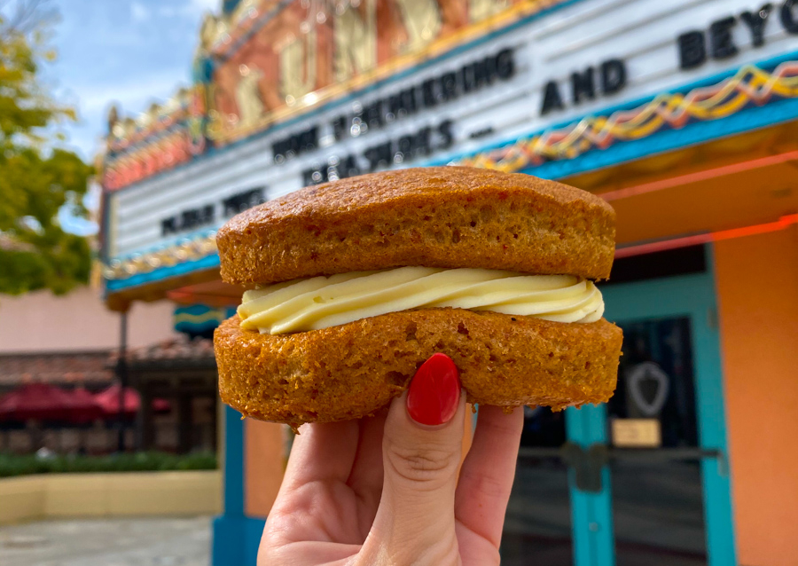 A woman holding up a carrot cake cookie infront of a builing in Disney World.