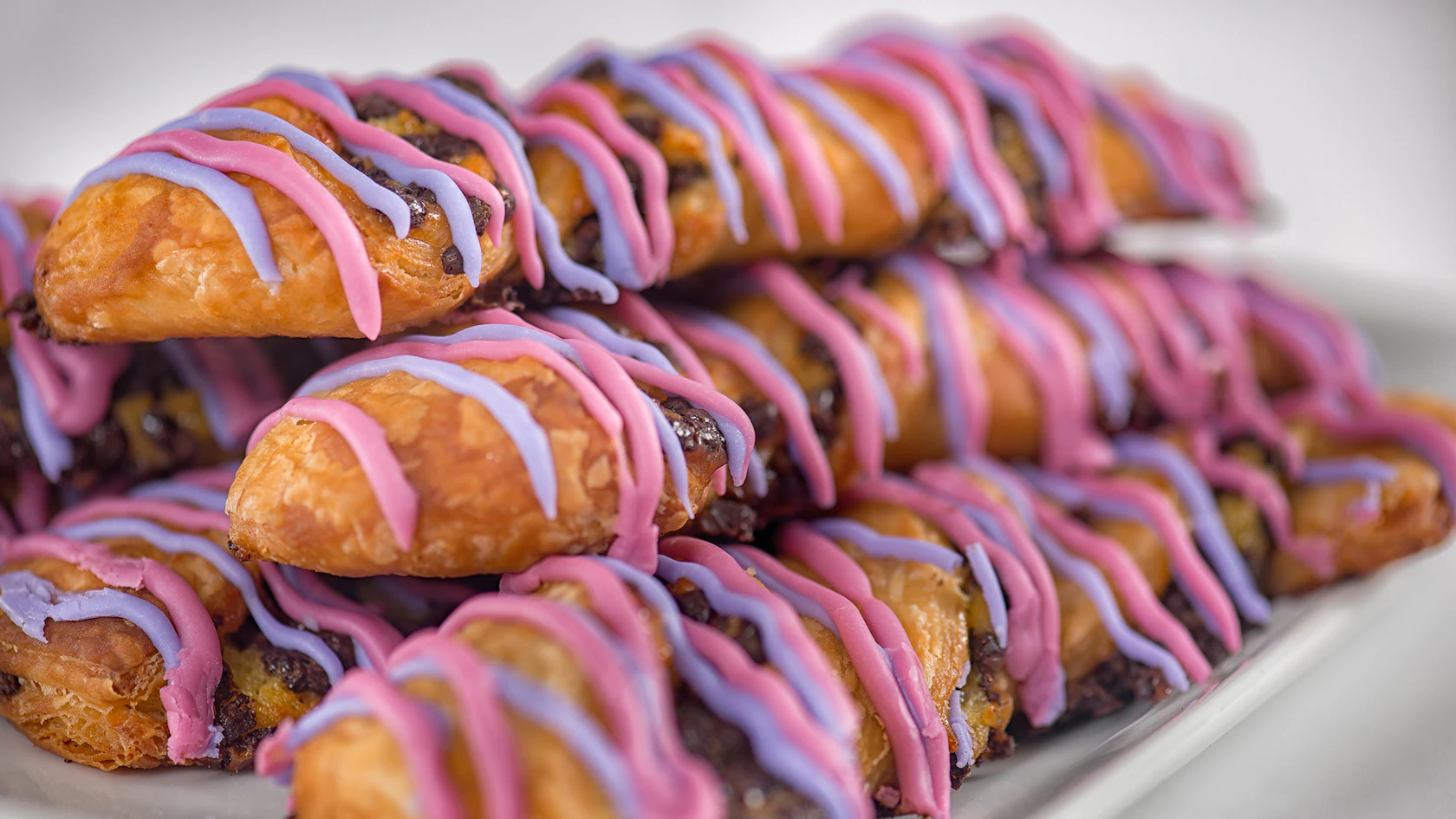 Picture of a stack of Cheshire Cat Tail snacks. Long pastry with blue and pink icing.