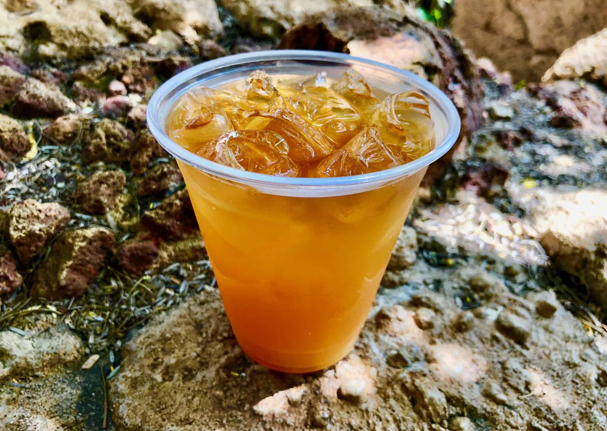 A plastic cup of ngumu jungle juice standing on a rock. The drink is orange in colour.