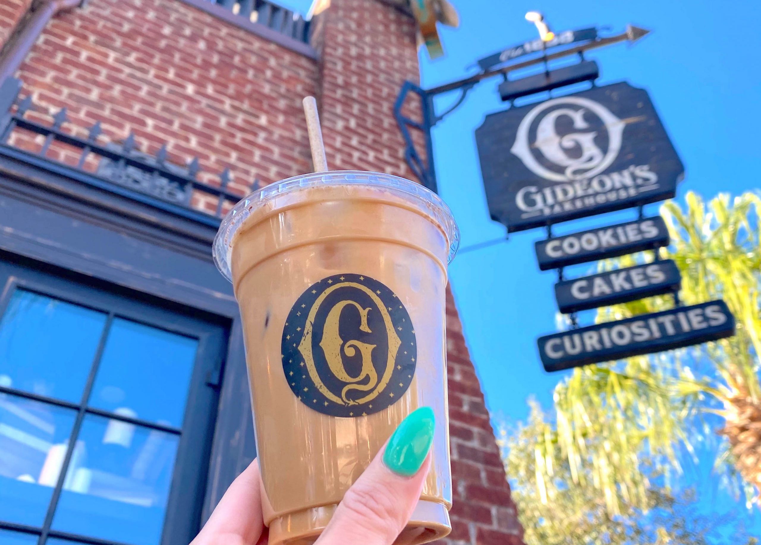 A brown coloured peanut butter cold brew in a plastic cup being held infront of the 'Gideons Bakehouse' sign.